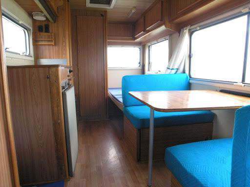 Blauwe zit- en rugkussens gerangschikt in het interieur van een caravan, met een kleine tafel ertussen