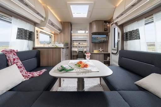 Drie zwarte kussens in U-vorm gerangschikt in het interieur van een caravan, met een kleine tafel in het midden